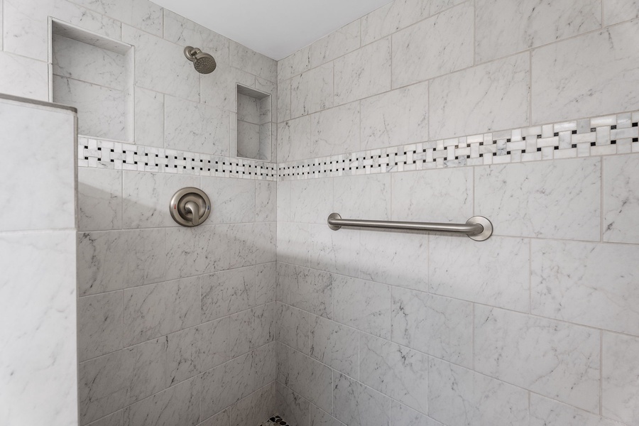 Walk-in shower with tiled walls and convenient grab bars.