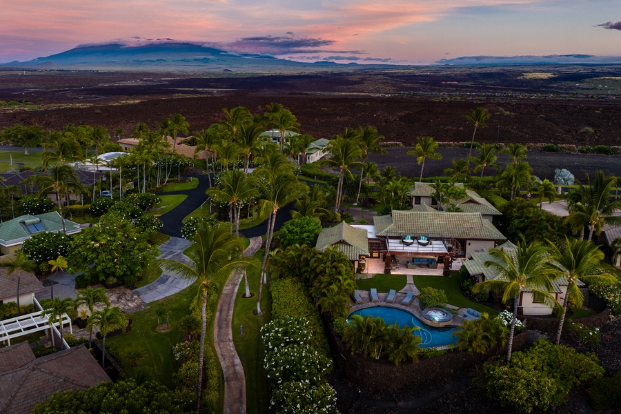 A serene sunset view of the property surrounded by lush greenery and a private pool.