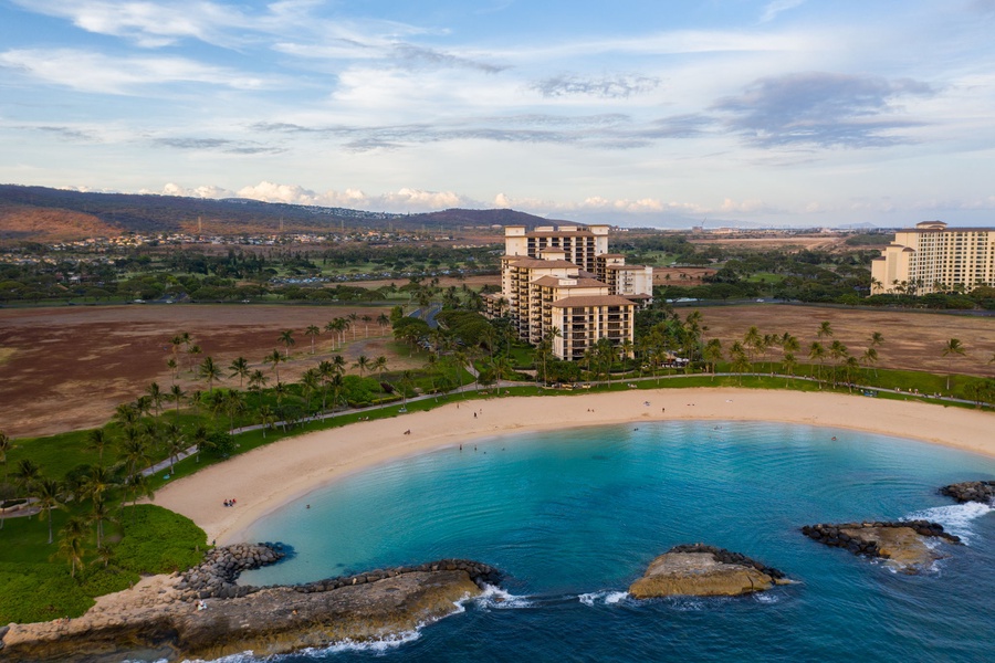 Aerial view of beachfront resort buildings and pristine lagoon with protected swimming area surrounded by natural landscape.