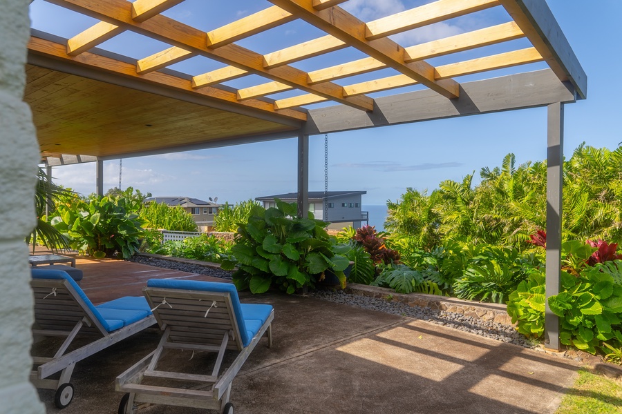 Relaxing lanai with lounge chairs under a pergola, surrounded by lush greenery and offering serene views.