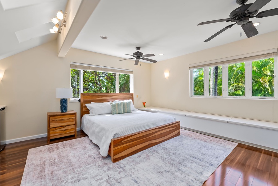 Wake up to lush tropical views through panoramic windows in your spacious bedroom, where warm wood tones and ceiling fans create perfect comfort.