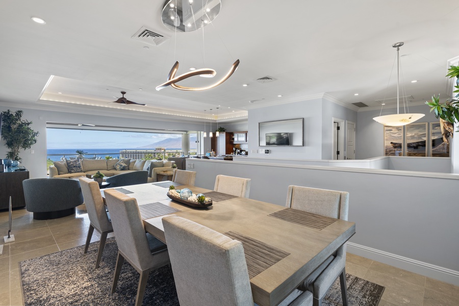 The elegant dining area features a contemporary chandelier and a spacious table, perfect for gathering with family and friends. The open layout seamlessly connects the dining room to the living area and kitchen, with breathtaking ocean views.