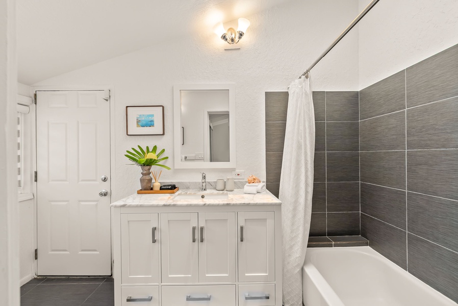Your private sanctuary features a sleek marble-topped vanity, refreshing shower-tub combo, and modern gray tile accents—all bathed in soft natural light to start your mornings right.