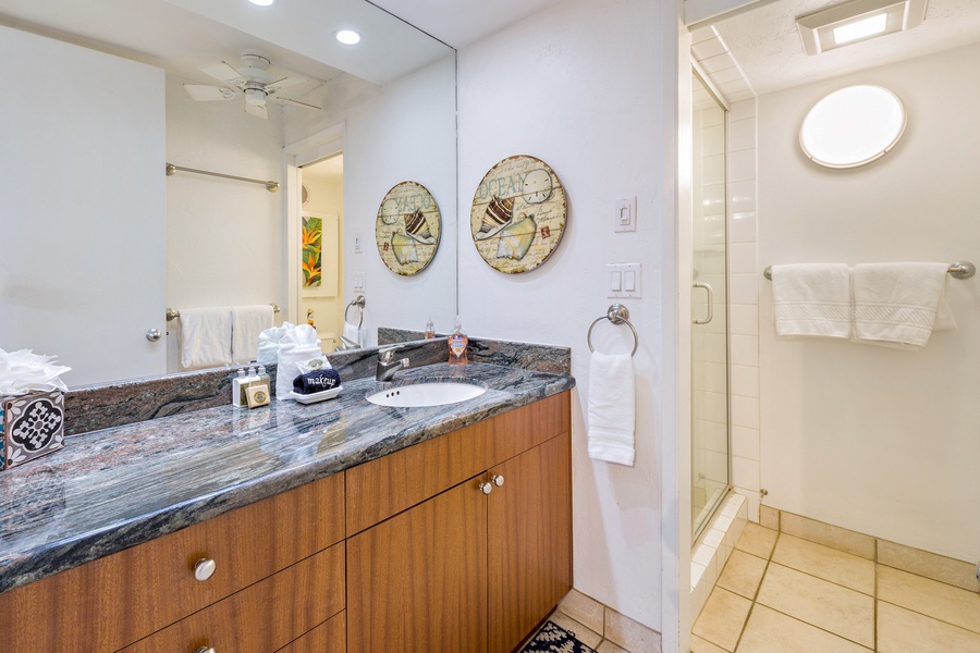 The bathroom in Papakea L-106 features a sleek granite vanity, accented by decorative wall pieces and soft lighting