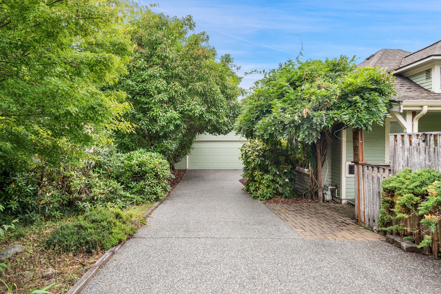 Tree-lined driveway leads to a charming property nestled among lush greenery in a peaceful residential setting.