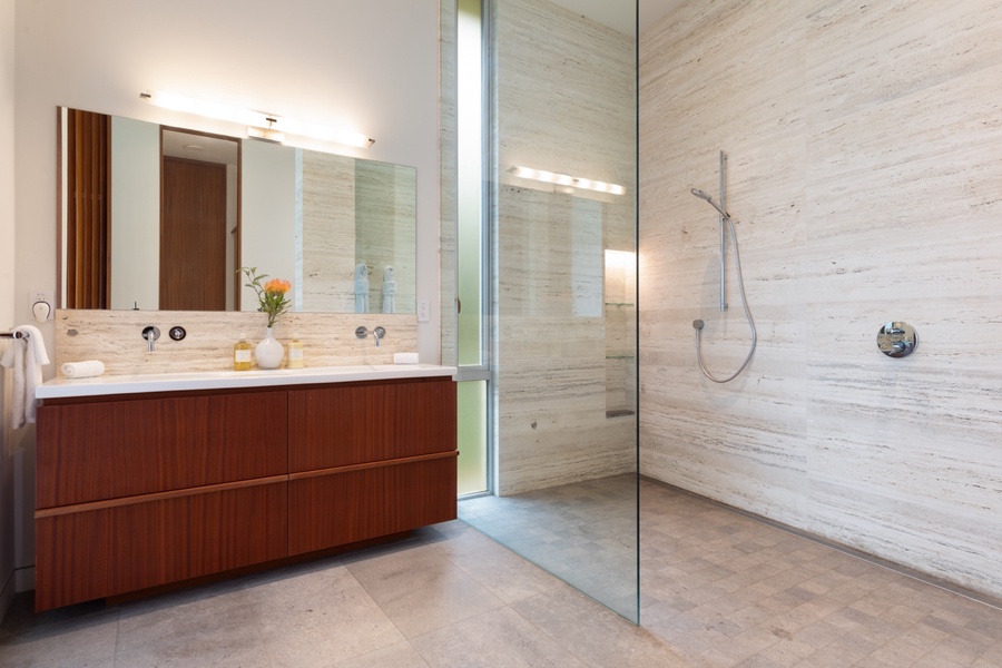 Elegant, spacious walk-in shower with natural stone tiles and a sleek wooden vanity.