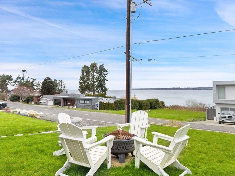Waterfront property features a charming fire pit seating area with Adirondack chairs overlooking the peaceful ocean and surrounding neighborhood.