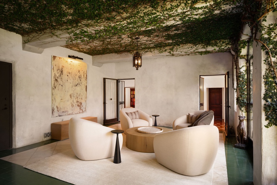 Lounge in this nature-wrapped living space where ivy overhead softens the ceiling and sculptural seating sets a serene mood.