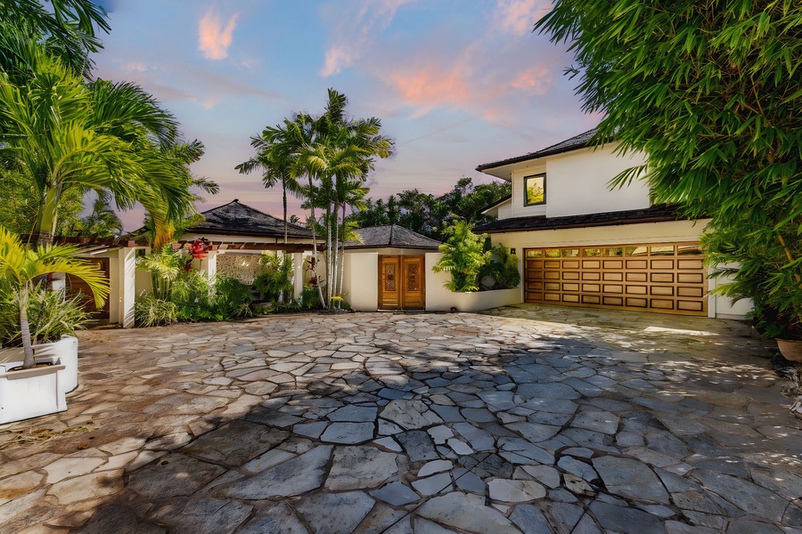 Stone driveway entrance lined with palms, arriving under soft sunset light.