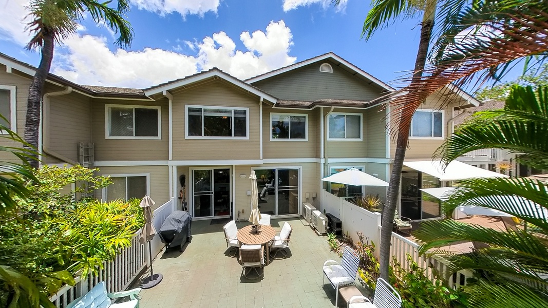 Two-story  featuring a spacious lanai with outdoor dining, surrounded by tropical palm trees in a sunny coastal setting.