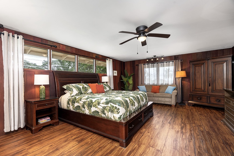 Unwind in your spacious primary suite with rich wood tones, a plush king bed, and a cozy seating area. High windows and tropical-inspired bedding create a serene, island-inspired retreat.