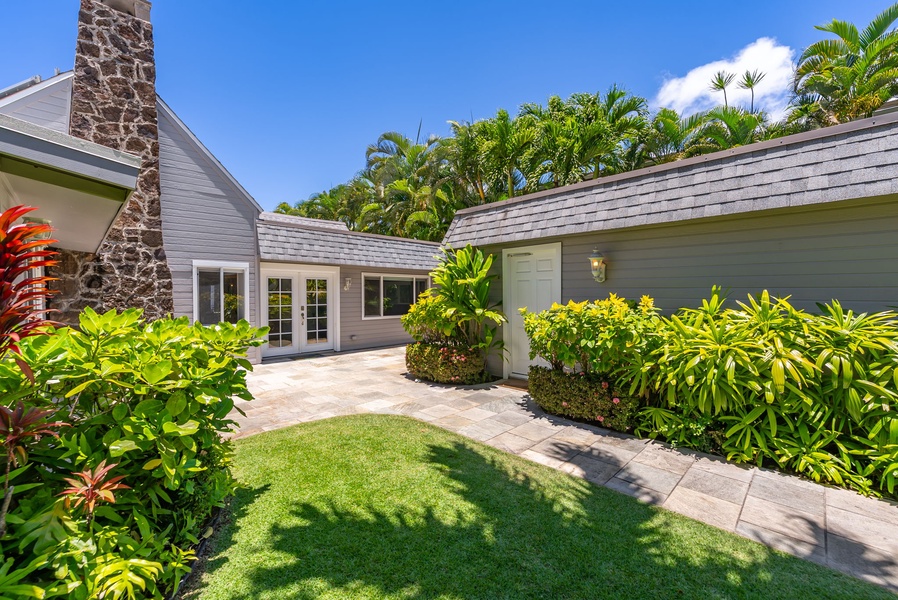 Charming property surrounded by lush tropical gardens under a brilliant blue sky, where a stone chimney and vibrant greenery create a serene island retreat.