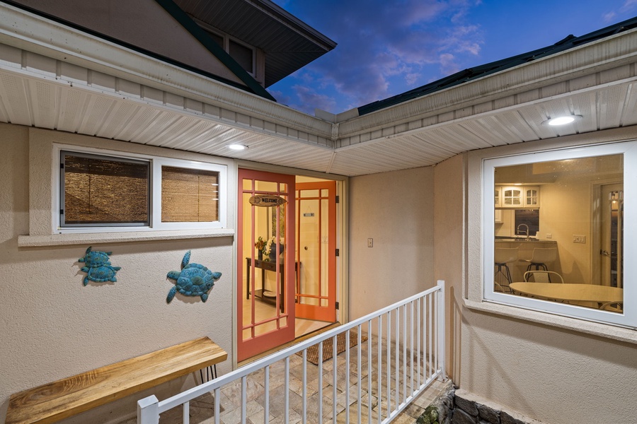 Property entrance showcasing a welcoming covered porch area with decorative turtle wall art and illuminated glass doors during twilight hours.
