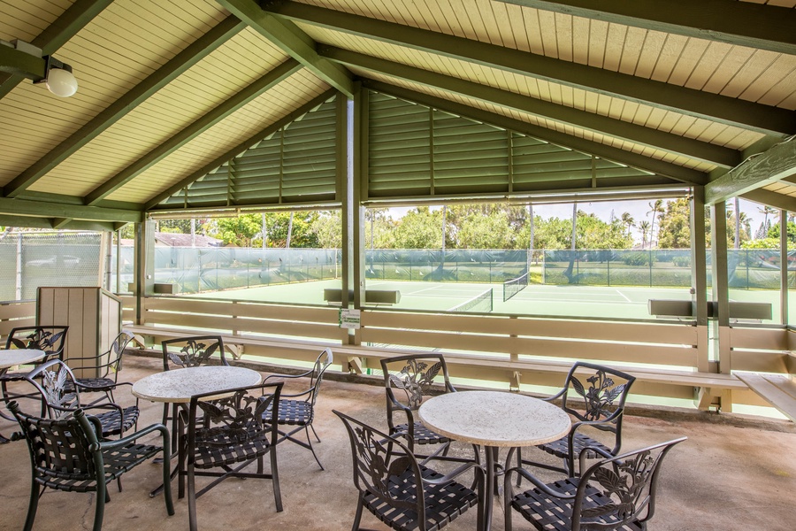 Covered pavilion with seating beside tennis courts.