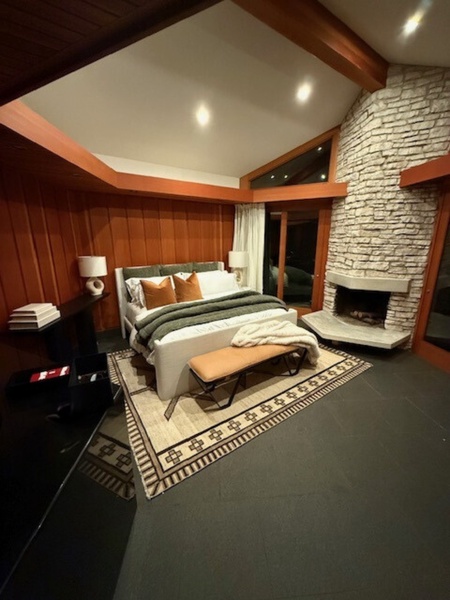 Cozy Primary Bedroom with a King-size bed, stone fireplace, and floor-to-ceiling windows for serene forest views.