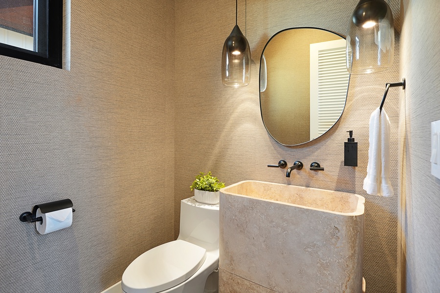 Stylish powder room with sculptural stone sink and statement lighting—an elevated touch of island-modern design.