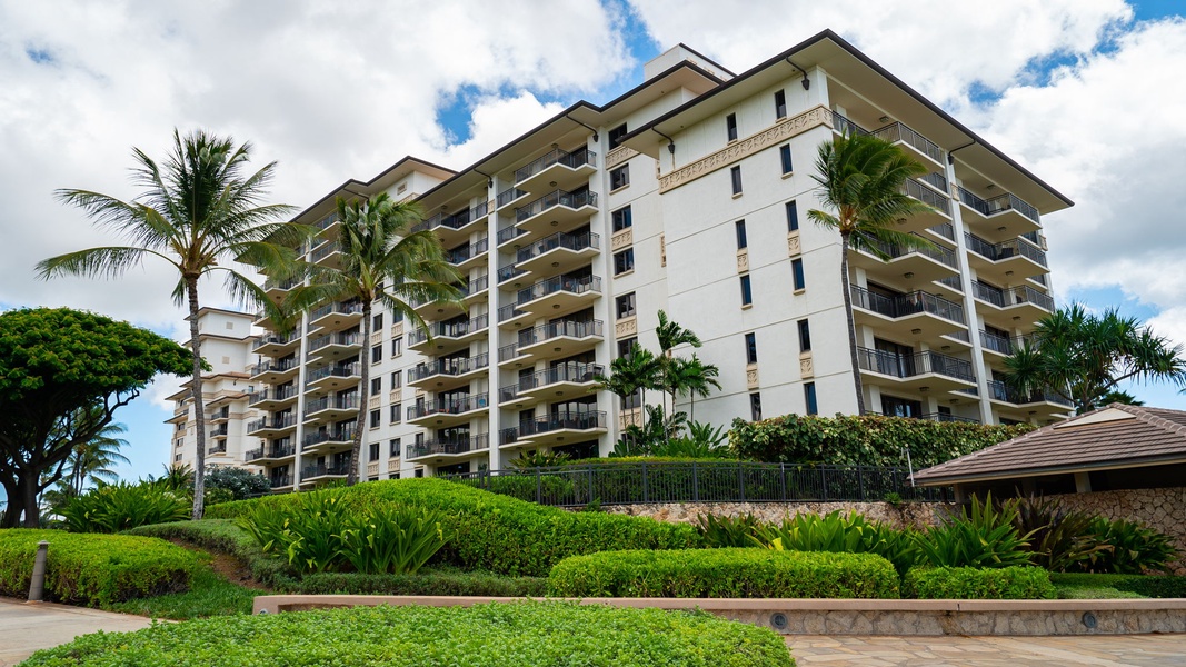 Modern beachfront condominium complex surrounded by lush tropical landscaping and swaying palm trees.