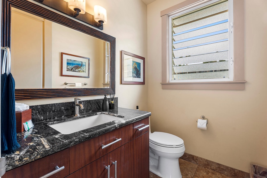 Stylish black-granite vanity and coastal artwork add flair to life’s little necessities.