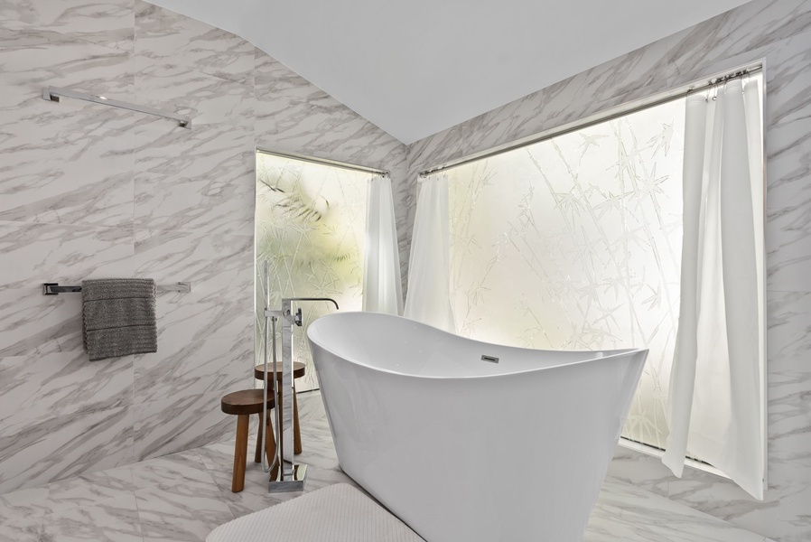 Freestanding tub set against marble walls, softly lit for a calming atmosphere.