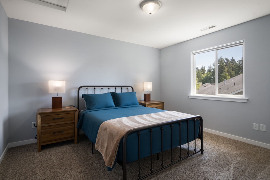 This welcoming guest bedroom features a cozy queen bed, soft natural light, and a peaceful residential view.