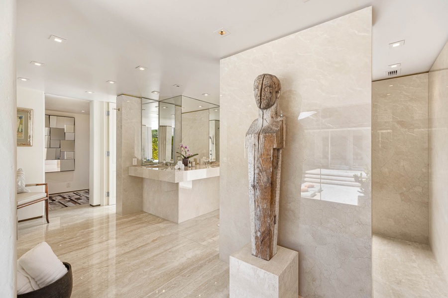 The serene statue stands as a testament to elegance, set against the expansive, reflective surface of the mirrors and the sophisticated textures of the bathroom.