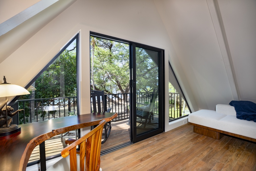 Loft area with a work desk and balcony access overlooking the surrounding greenery.