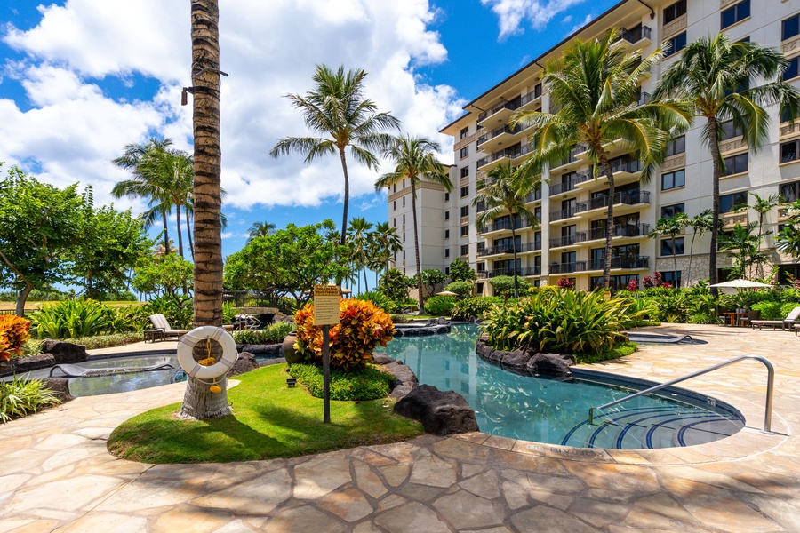 Resort pool area surrounded by lush tropical landscaping and palm trees under blue Hawaiian skies.