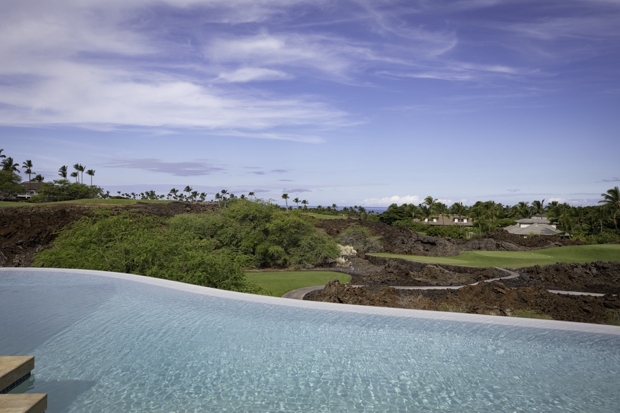 Infinity pool overlooking lush golf course and tropical landscape beneath stunning Hawaiian skies.