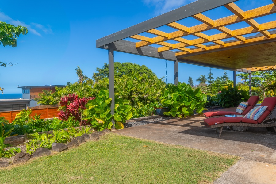 Relaxing lanai with lounge chairs under a pergola, surrounded by lush greenery and offering serene views.