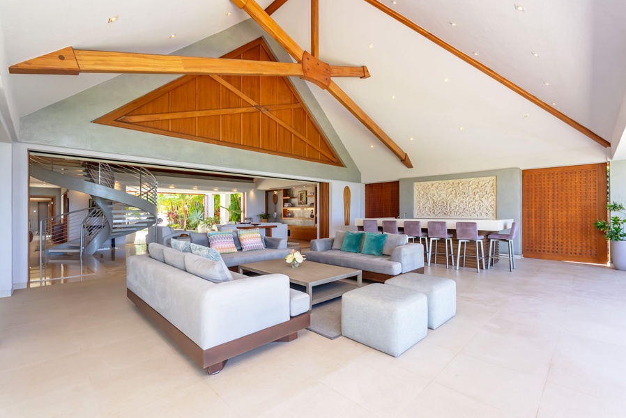 Soaring ceilings with stunning wood beams frame your open-concept living space, where plush seating, a sleek dining area, and tropical garden views create the perfect backdrop for relaxation and entertaining.