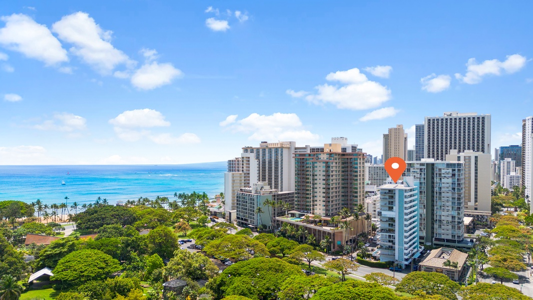 Panoramic view of a vibrant neighborhood with modern high-rise buildings set against a backdrop of the ocean and lush greenery.