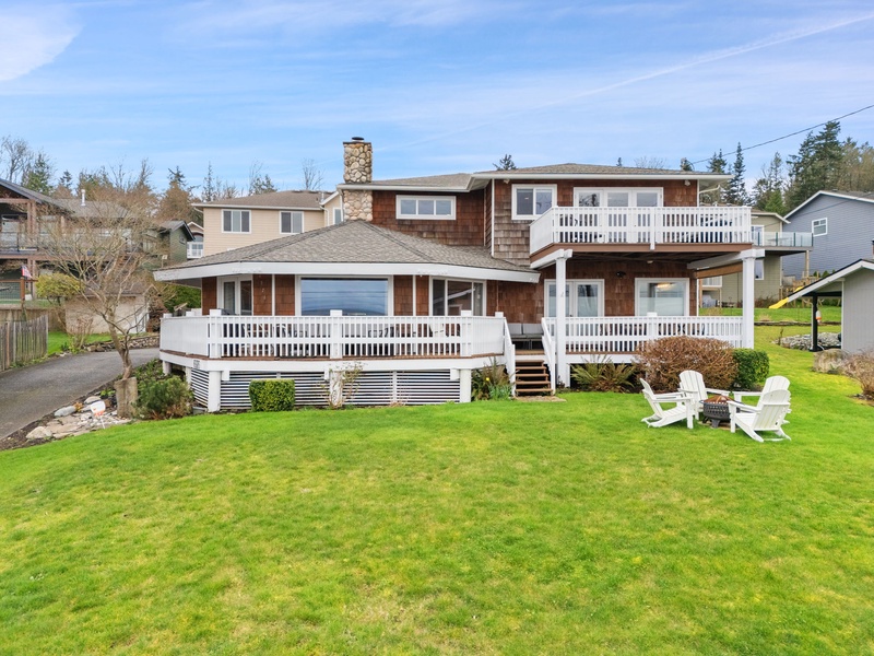 Charming two-story property featuring wraparound deck and spacious lawn in peaceful residential neighborhood.