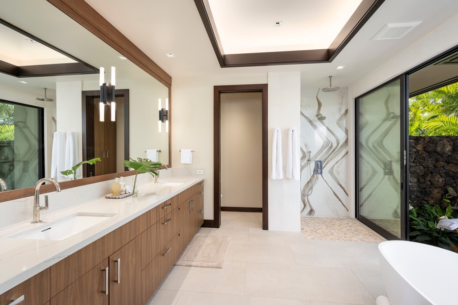 Primary Suite #1: Your luxurious bathroom sanctuary features dual vanities, a rainfall shower, and serene garden views through floor-to-ceiling windows.