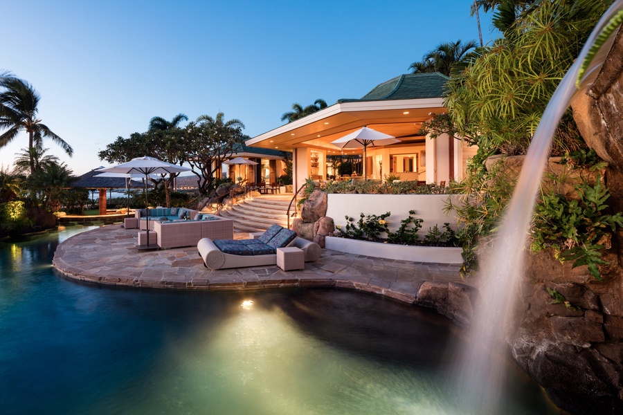 Palatial estate home at twilight with private pool, waterfall, and jacuzzi grotto.