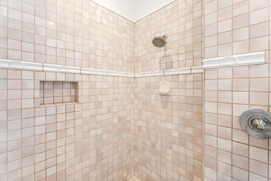 Neutral-toned walk-in shower with built-in shelves, blending convenience with clean, tropical-inspired tilework.