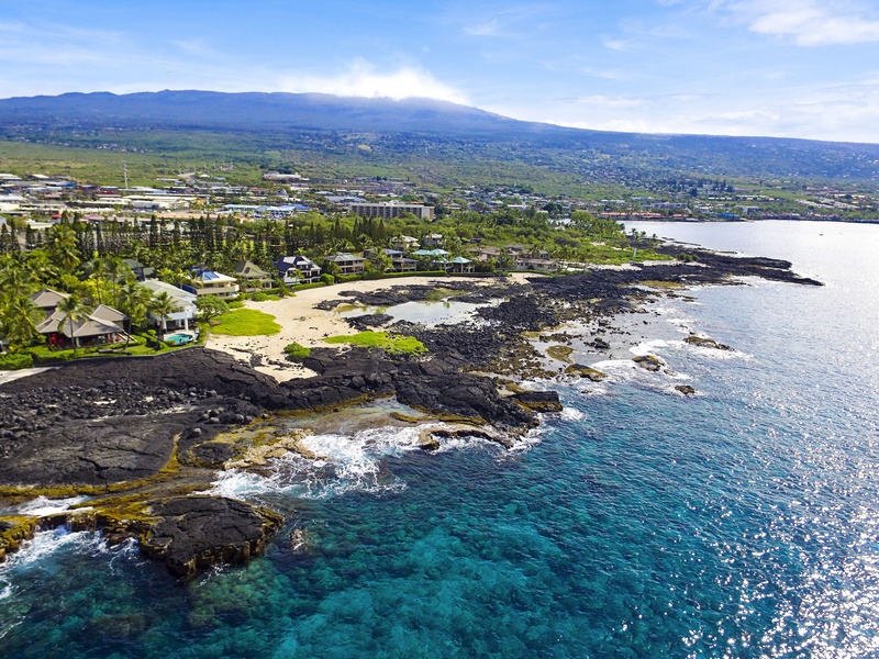 Aerial view reveals the volcanic coastline and vibrant blue waters below.