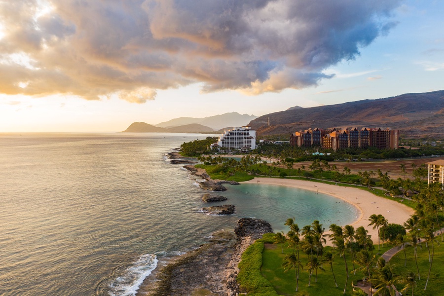 Stunning aerial view of the tropical coastline with pristine beaches and resort buildings nestled between ocean and mountains at golden hour.
