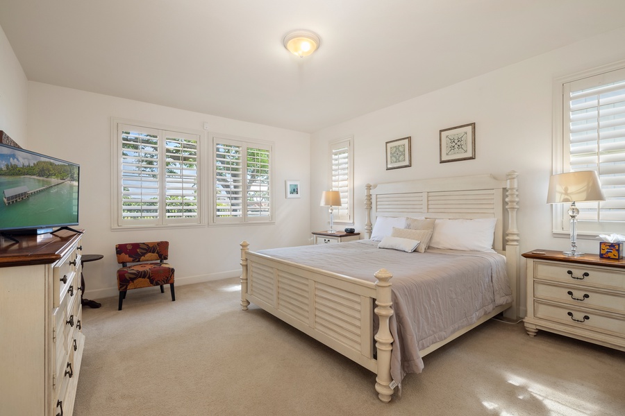 Your peaceful bedroom retreat features crisp white linens and plantation shutters that filter gentle morning light across polished floors.