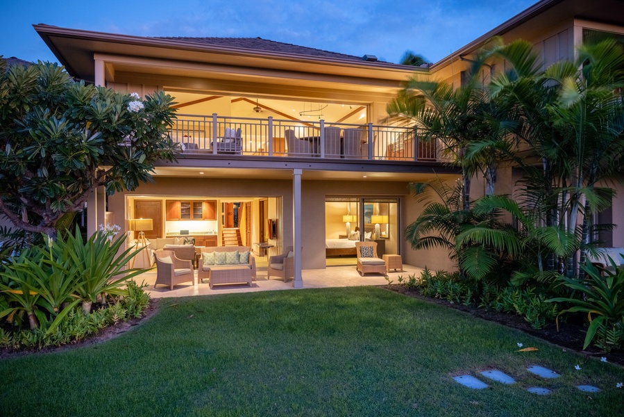 Back of this spacious home at twilight, showcasing upper and lower decks and grassy lawn.