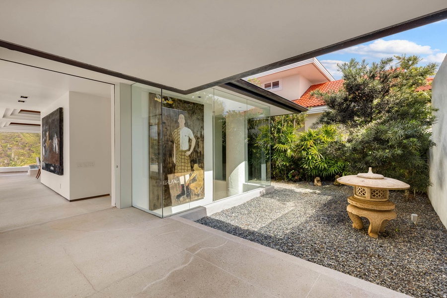 A serene courtyard space features a clear glass-walled room, allowing unobstructed views of a showcased art piece.