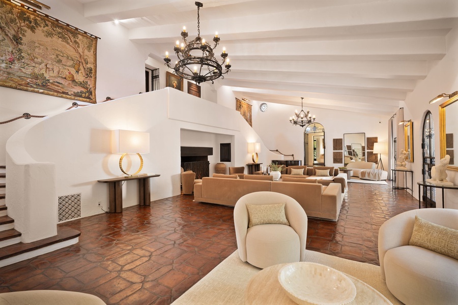 Gather in the grand 52-foot living room, where soaring ceilings, wrought-iron chandeliers, and warm terracotta floors create a dramatic yet welcoming retreat.