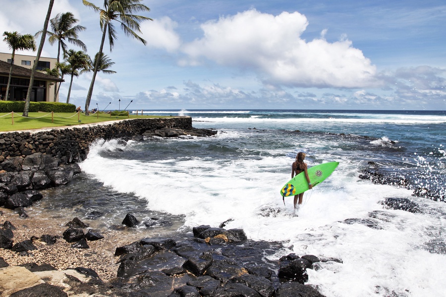 Watch surfers ride waves against a rocky shoreline.