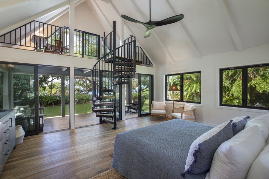 Open loft-style primary bedroom featuring high ceilings, a spiral staircase, and forest views.