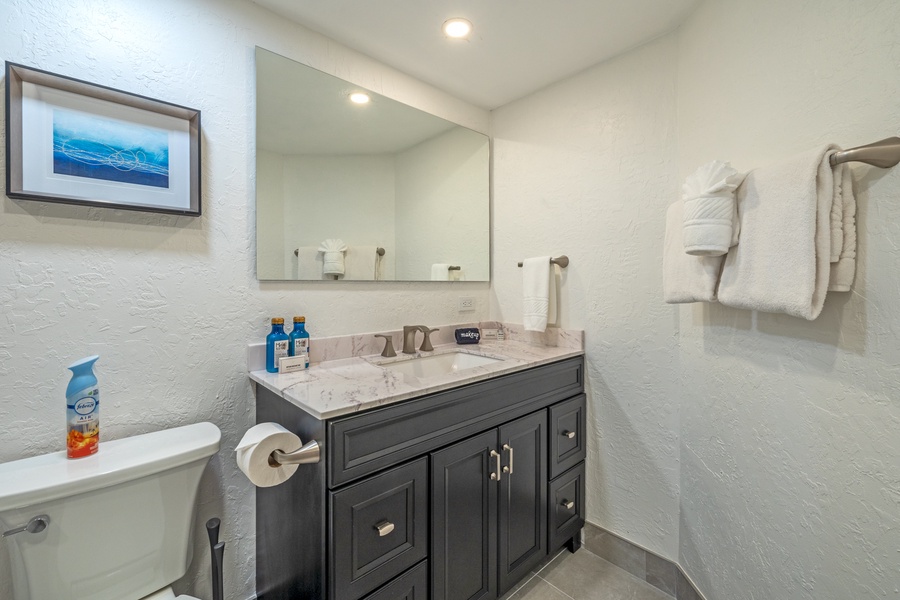 Well-lit bathroom at Kaanapali Shores 213, with dark wood vanity and a wide mirror that reflects the warm ambiance.