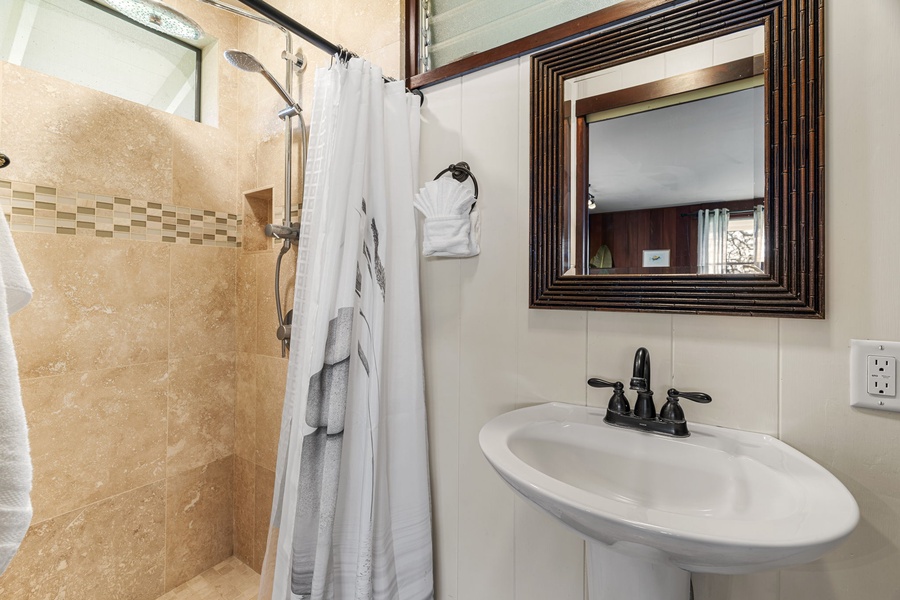 Step into your private bathroom, where warm beige tones and fresh white linens create a serene retreat. The shower awaits with fluffy towels ready, and a handsome framed mirror adds an elegant touch above the sink.