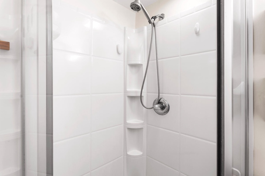 Step into your pristine white-tiled shower with modern fixtures and built-in corner shelving for your essentials.