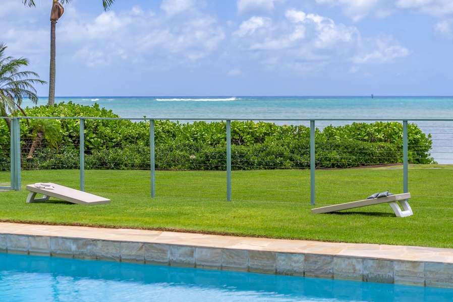 A tranquil waterfront retreat with a sparkling pool framed by lush lawn, swaying palms, and endless turquoise ocean views just beyond.