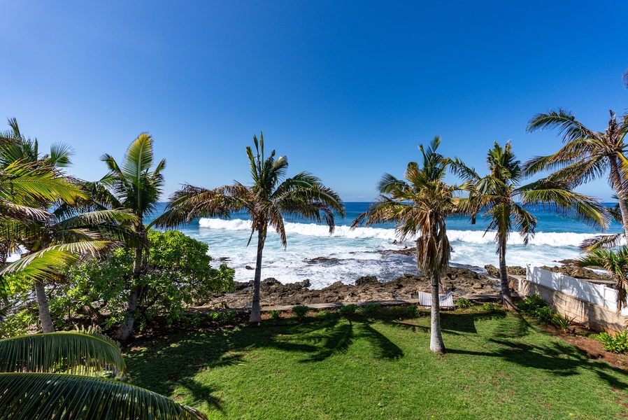 Oceanfront lawn and lava rocks frame the view in front of the home.