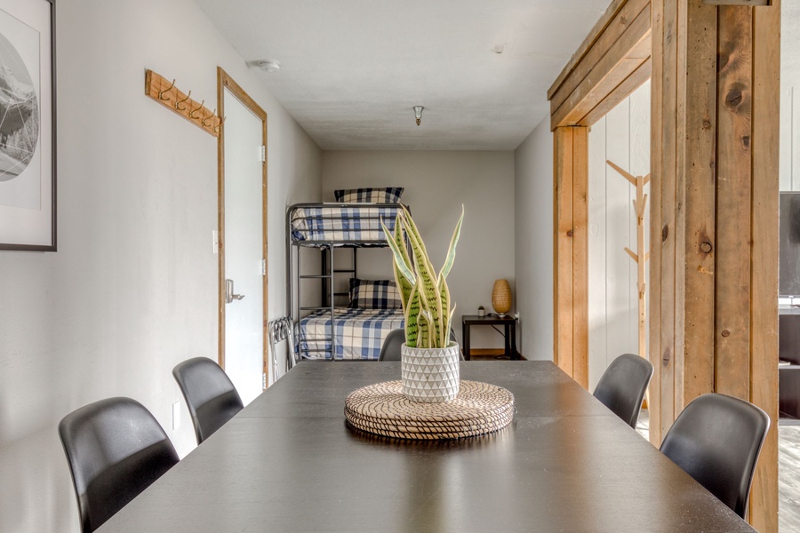 A dining table that seats 6 and a 2-stool high-top bar rests opposite a sleeping nook where a twin-over-full bunk bed can be found.