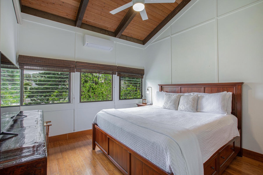 Primary suite with king bed, A/C, and picture windows framing tropical greenery.